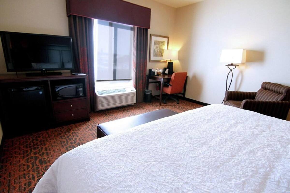 Une chambre d’hôtel comprenant un lit, un bureau avec une chaise, une télévision, un four à micro-ondes et une fenêtre avec des rideaux.
