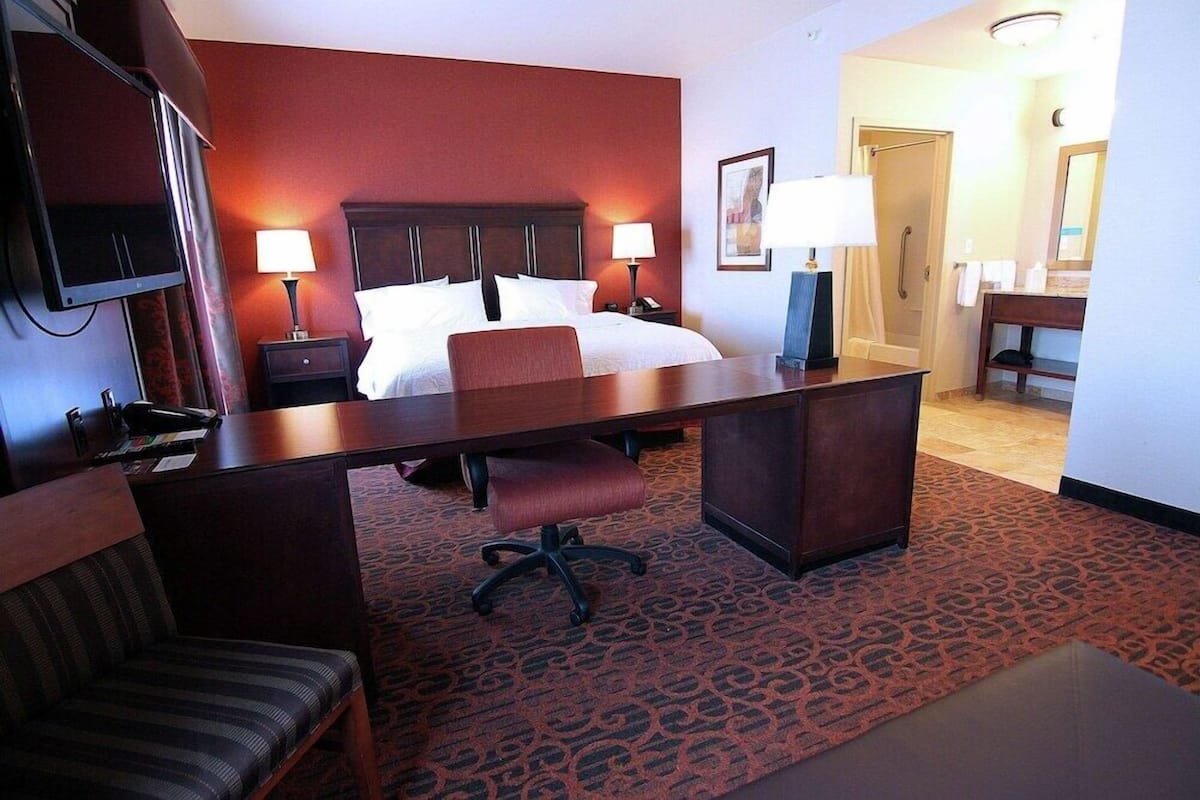 A hotel room with a bed, desk, chair, TV, and a bathroom visible in the background.