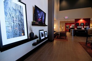 A hotel lobby with a flat-screen TV, framed artwork, and a reception area with a red wall and coffee machines.