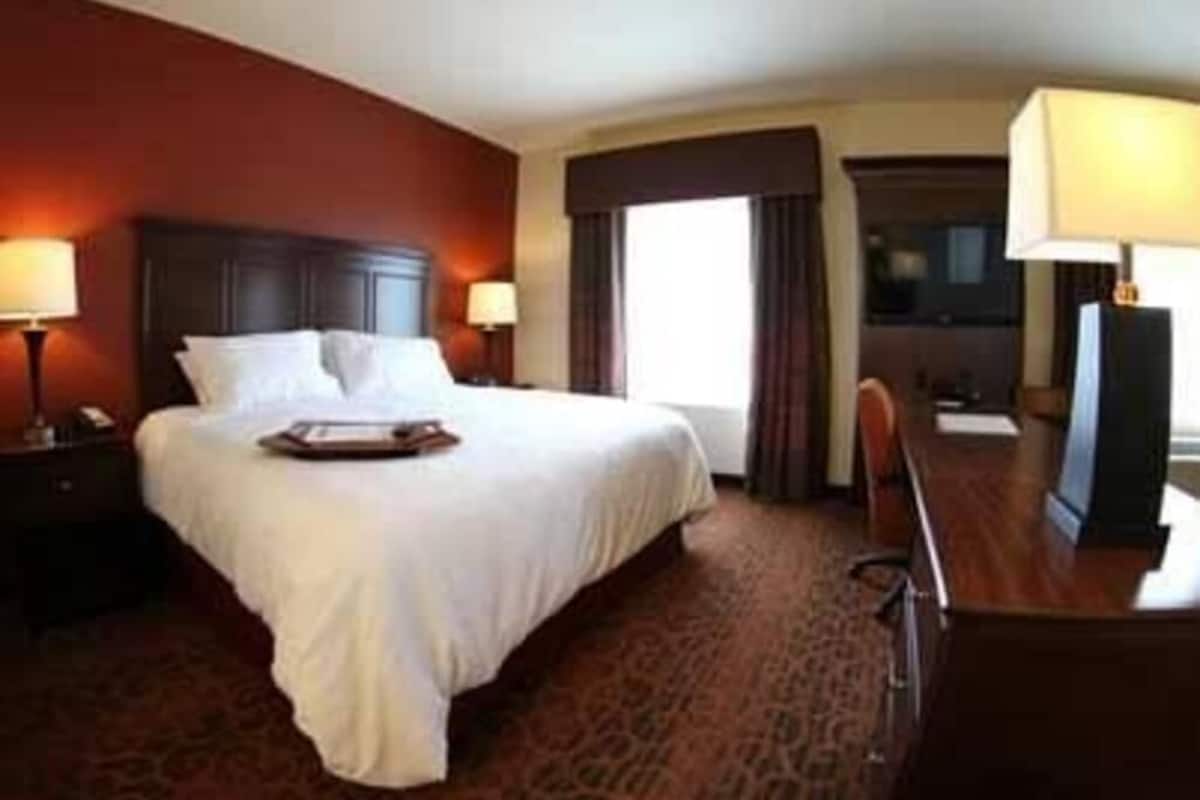 Une chambre d’hôtel avec un grand lit, deux tables de chevet avec des lampes, un bureau avec une chaise et une fenêtre avec des rideaux.
