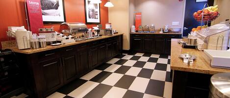 A kitchen with a checkered floor, a coffee station, and a fruit basket.