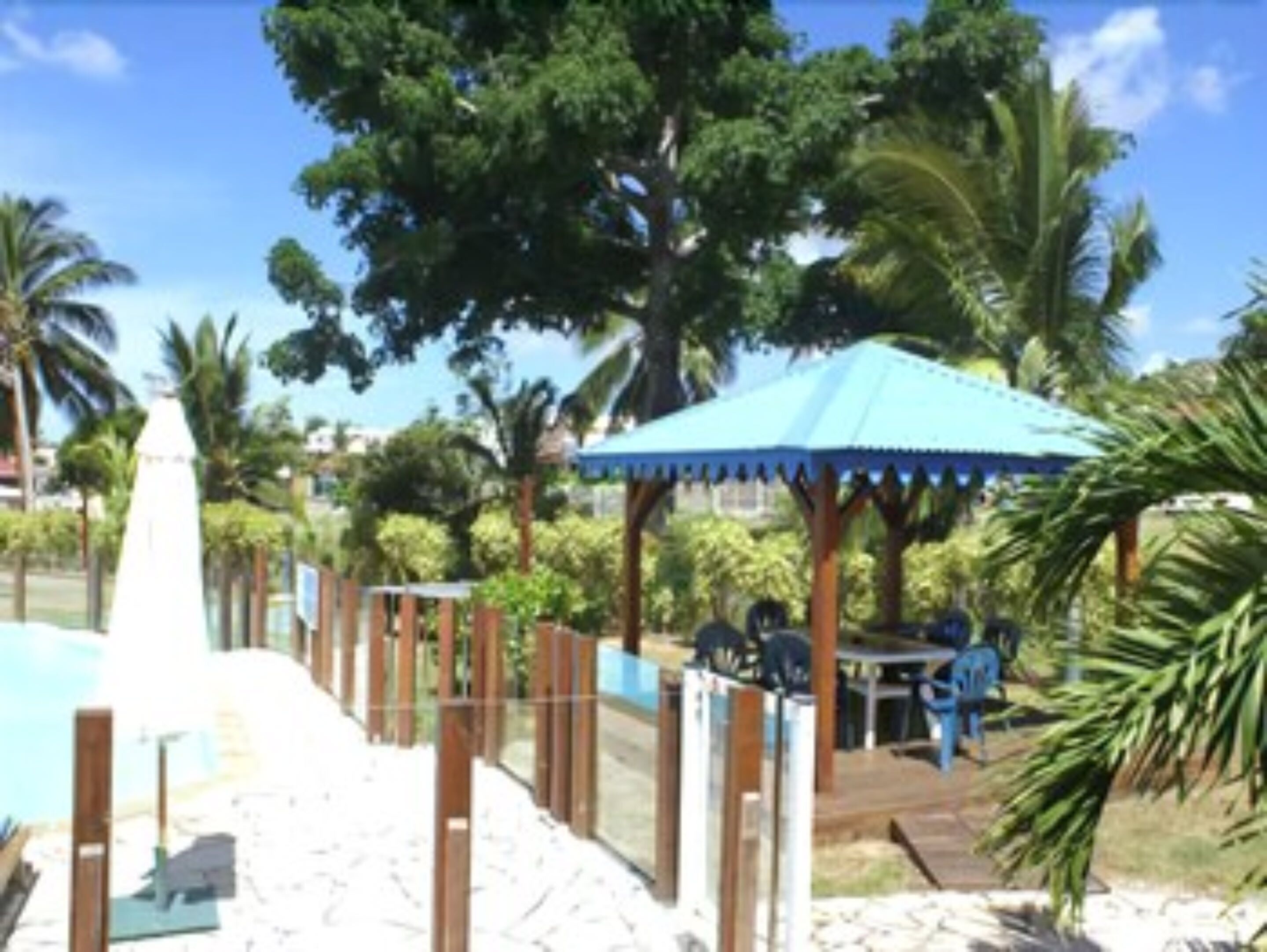 A pool area with a wooden fence, a gazebo, and palm trees.