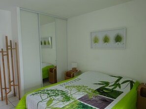 A bedroom with a bed, a bedside table, a nightstand, a mirror, and a wooden partition.