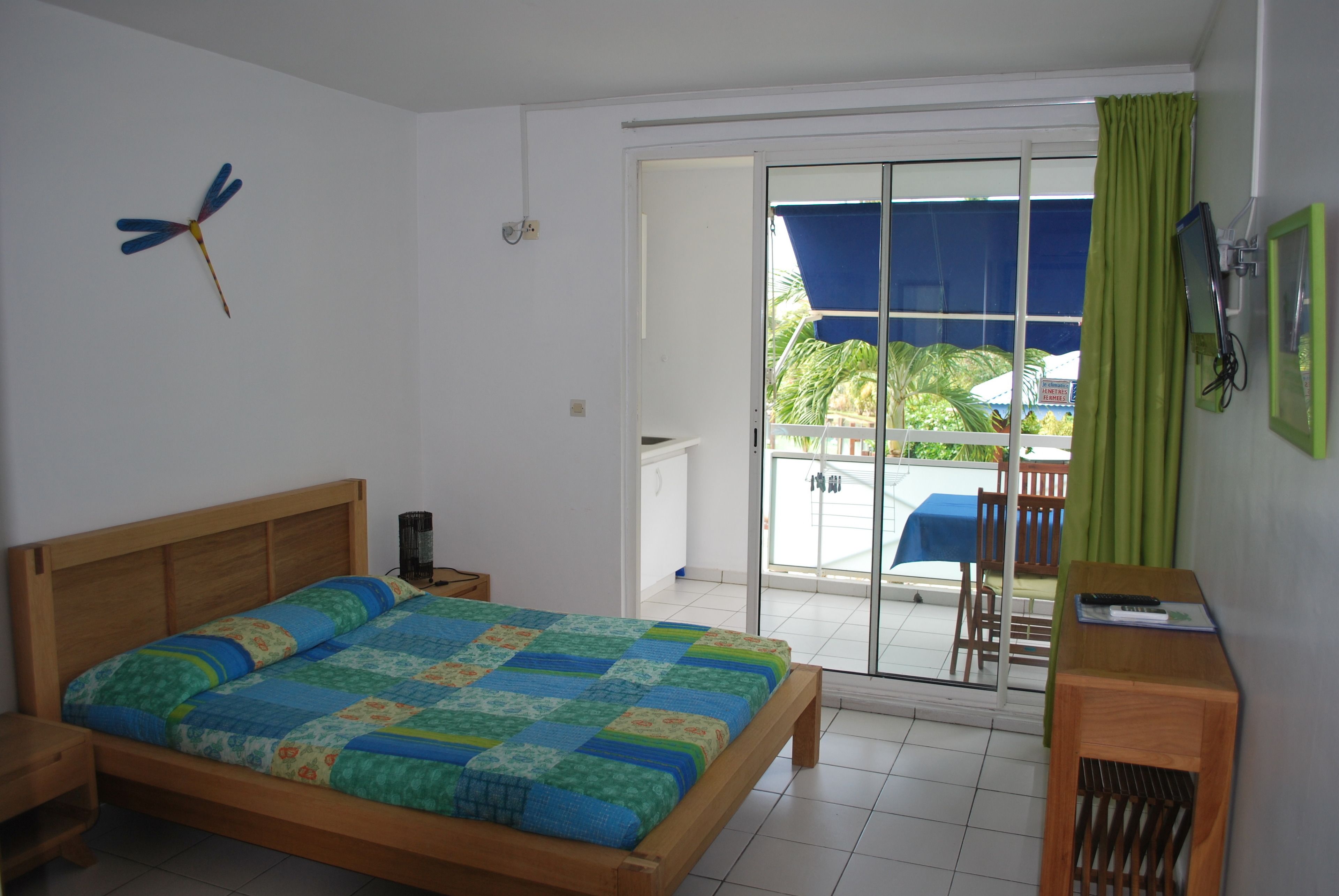 A bedroom with a wooden bed, a nightstand, a wall-mounted lamp, and a view of the outside balcony.