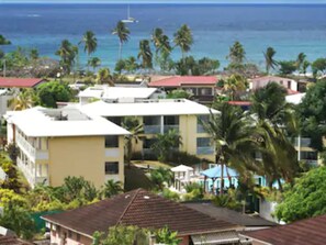 A coastal residential area with multiple buildings, some with red roofs and others with white. There are palm trees and a view of the ocean. - Les Créolines (Sainte-Luce)