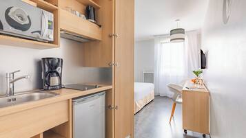 Une chambre d’hôtel compacte comprenant un coin cuisine, un lit, un bureau et une petite salle de bain.