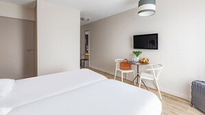 Una habitación de hotel con una cama, un escritorio con una silla, un televisor y una maleta.