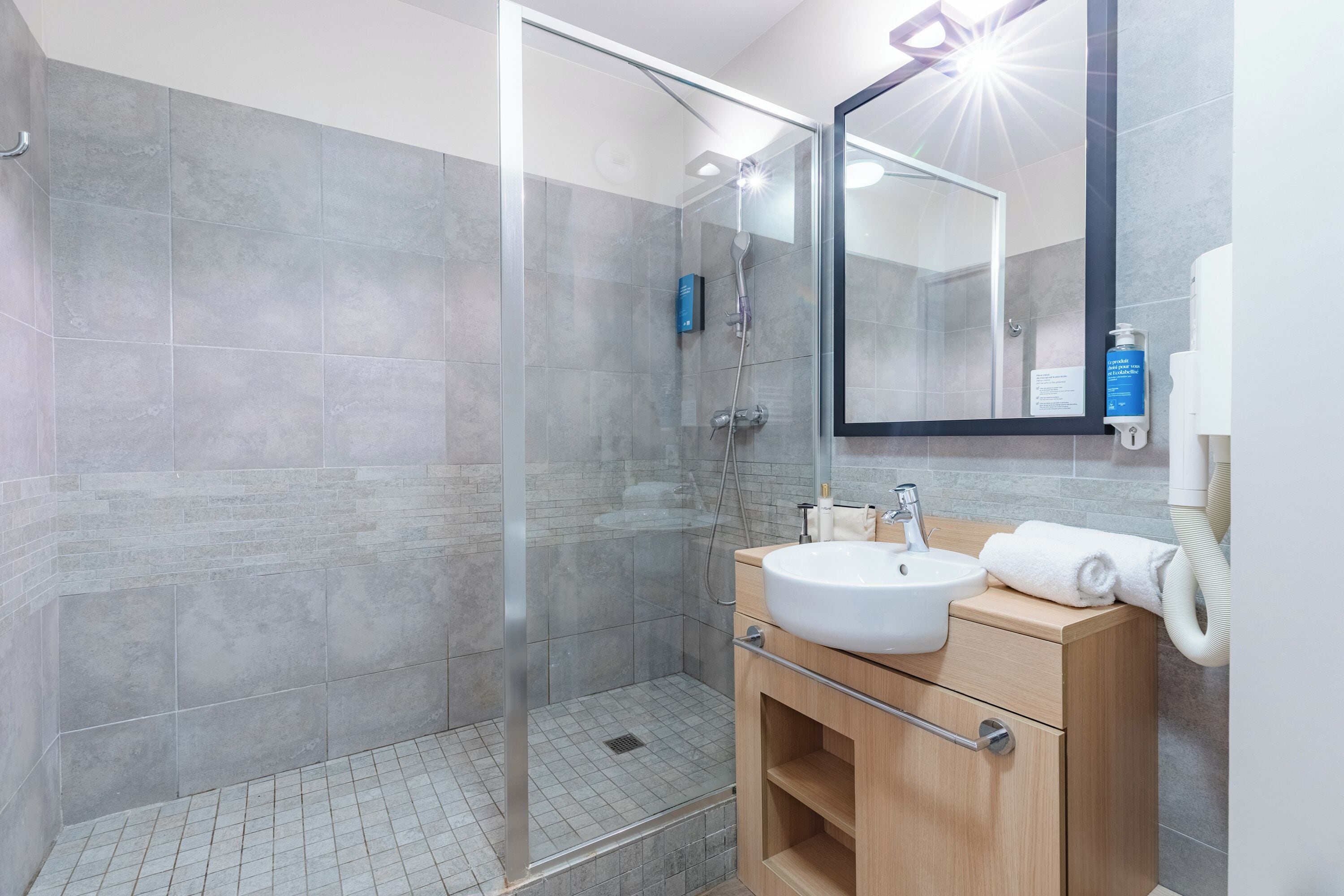 Une salle de bain moderne avec une douche à parois de verre, un meuble-lavabo en bois et un miroir.