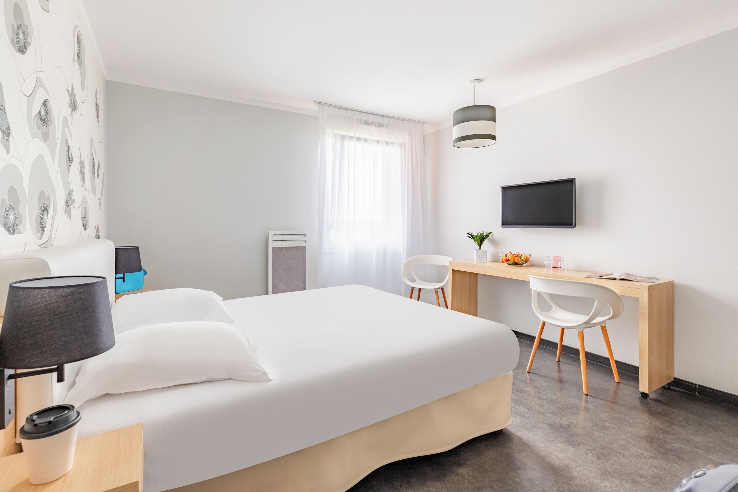 A modern hotel room with a bed, desk, chairs, and a TV.