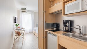Una cocina compacta con microondas integrado, cafetera y lavavajillas. Hay un comedor con una mesa y sillas.
