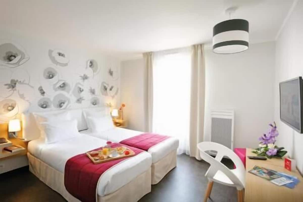 A hotel room with two beds, a desk with a chair, a TV, and a window with curtains.