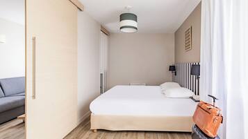 A hotel room with a bed, a grey sofa, a suitcase, and a handbag.