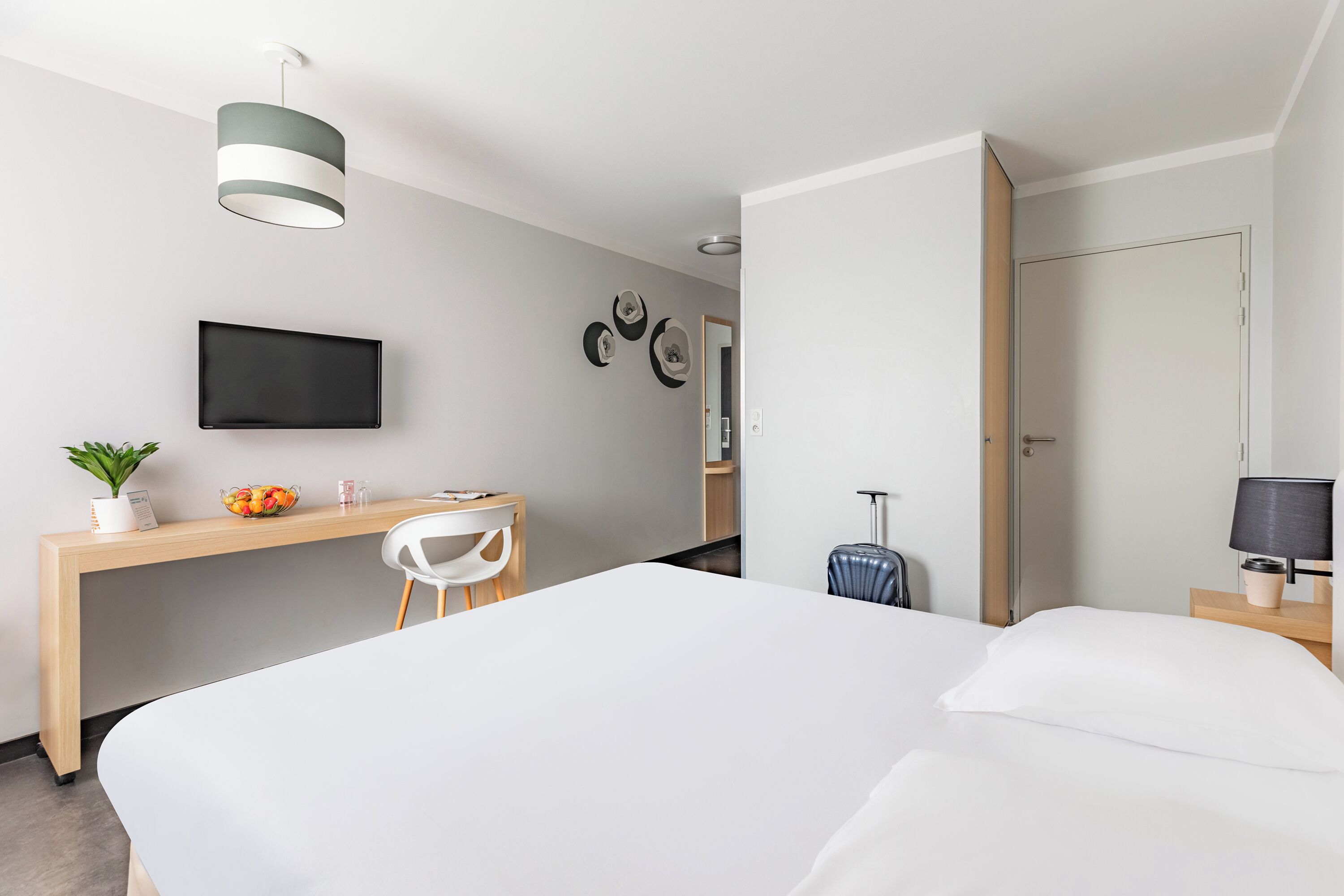Una habitación de hotel con cama, escritorio, silla, televisor, lámpara y maleta.