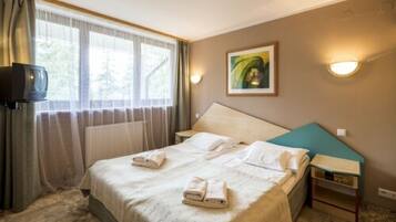 A hotel room with a bed, a bedside table, a TV, and a painting on the wall.