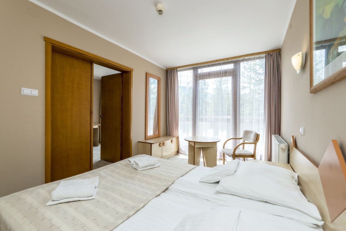 Une chambre d’hôtel avec un lit, une chaise, une petite table et une fenêtre avec des rideaux.
