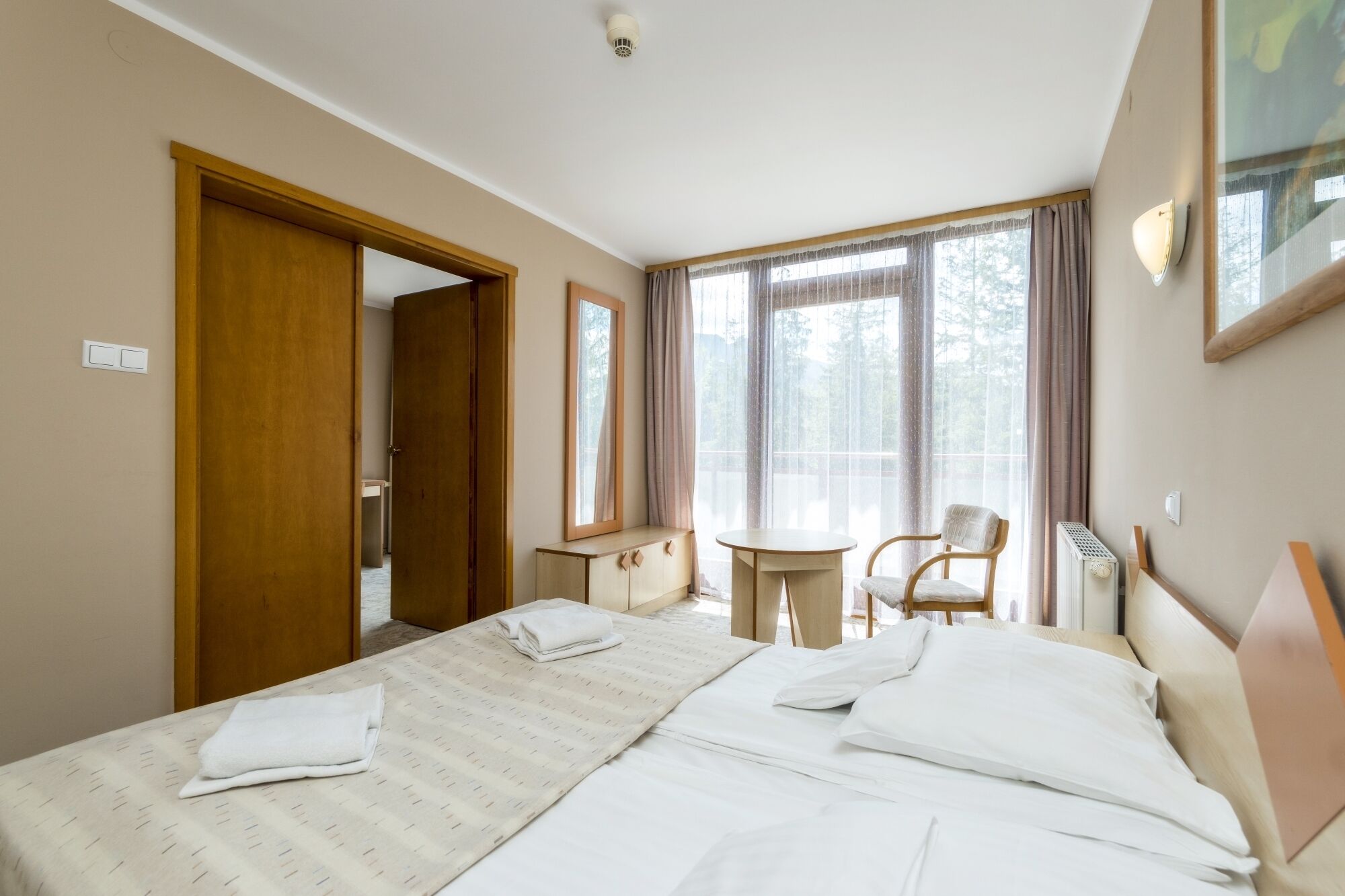 Una habitación de hotel con cama, una silla, una mesita y una ventana con cortinas.