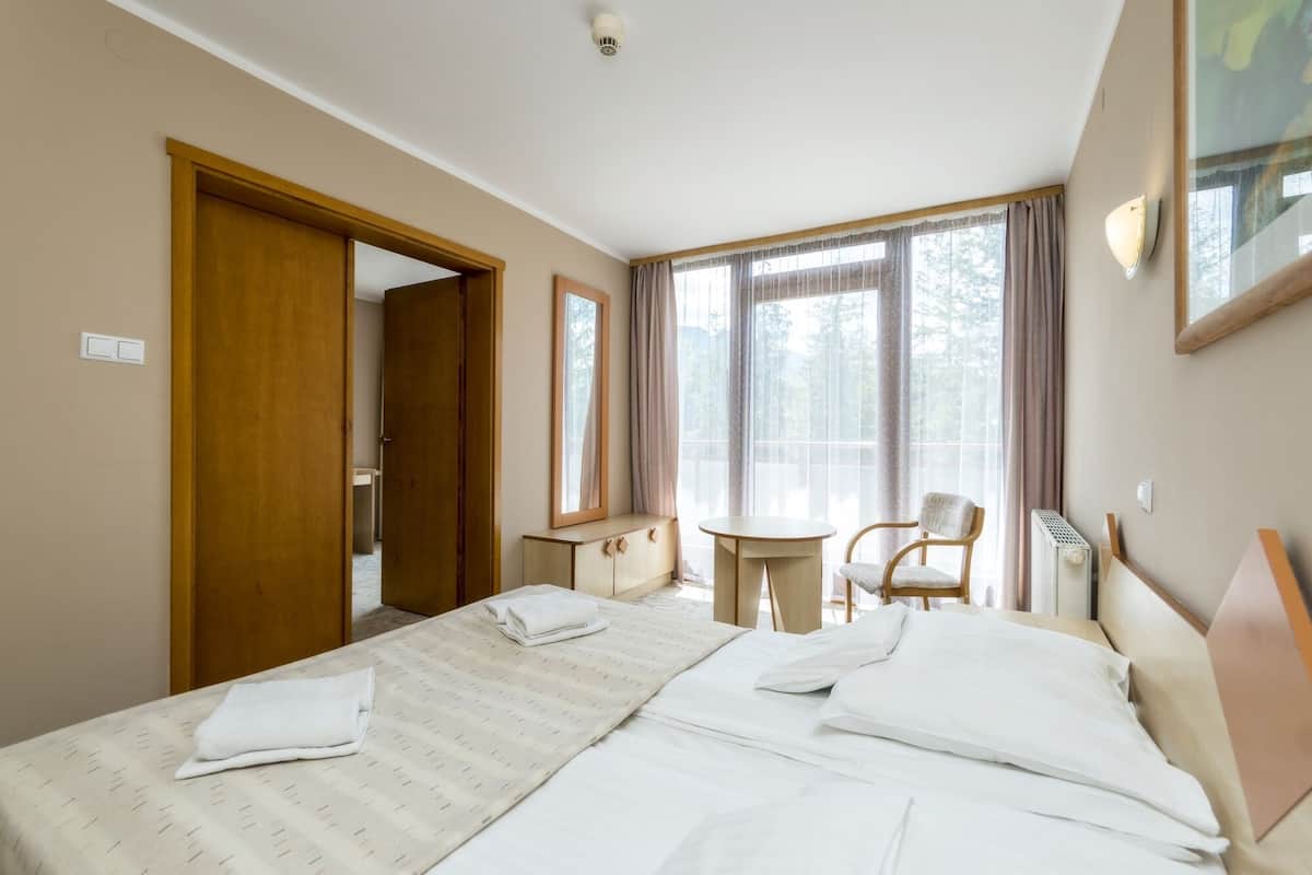 Een hotelkamer met een bed, een stoel, een klein tafeltje en een raam met gordijnen.
