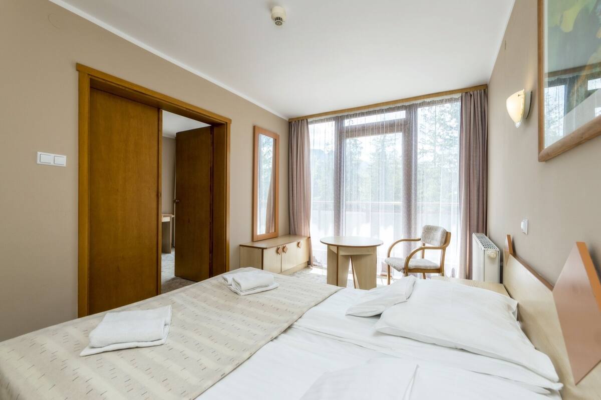 Una habitación de hotel con cama, una silla, una mesita y una ventana con cortinas.