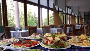 Een buffet met diverse gerechten, zoals salades, groenten en pasta, gepresenteerd in een eetruimte met tafels en stoelen.
