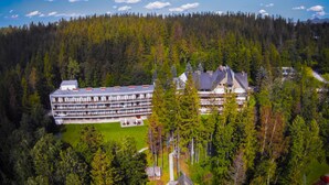 Een groot hotel met meerdere verdiepingen en een centrale binnenplaats, omgeven door dicht bos en bergen.