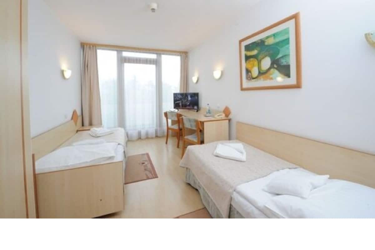 Een hotelkamer met twee eenpersoonsbedden, een bureau met stoel, een televisie en een schilderij aan de muur.