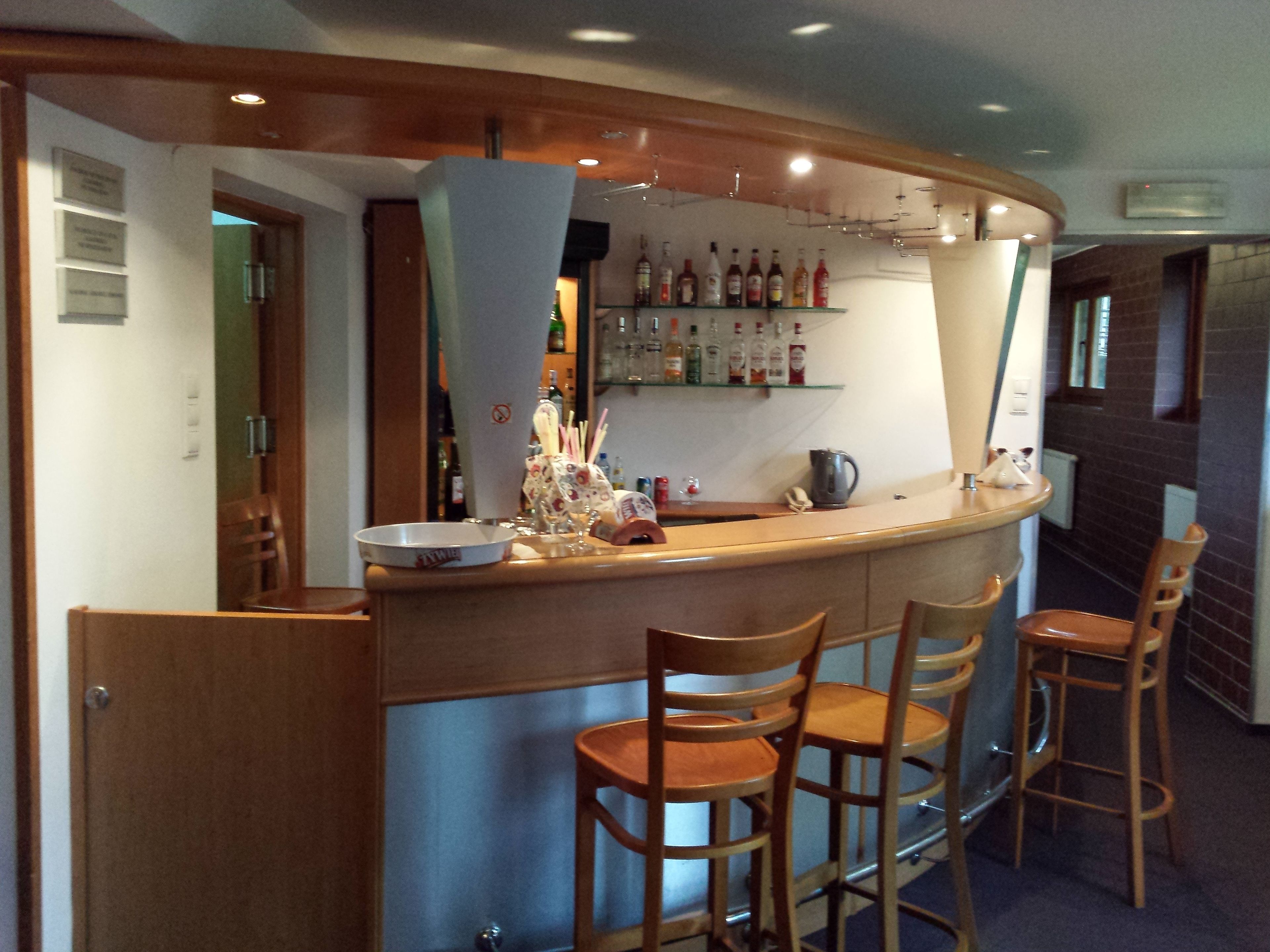 A bar area with a curved counter, wooden chairs, and shelves stocked with bottles.