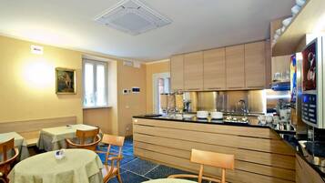 Habitación de hotel compacta con kitchenette, comedor con mesas y sillas, y una cama individual.