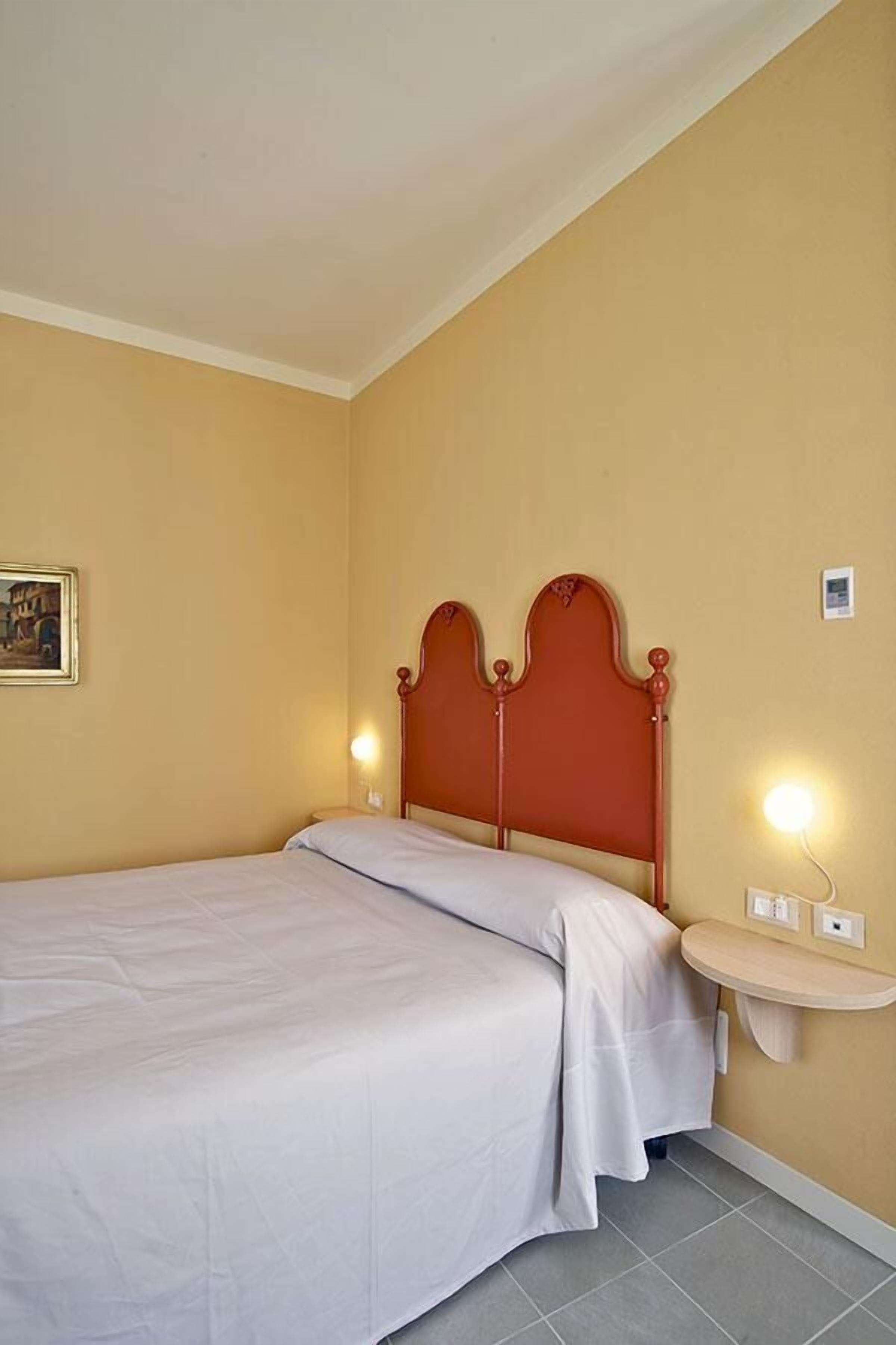 A single bed with a wooden headboard, a bedside table with a lamp, and a wall-mounted light fixture.