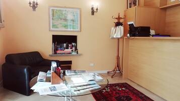 A living room with a black leather sofa, a glass coffee table with magazines, a red patterned rug, a wooden cabinet, and a map on the wall.