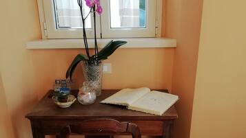 A wooden desk with a vase of pink orchids, a notebook, and a small potted plant.
