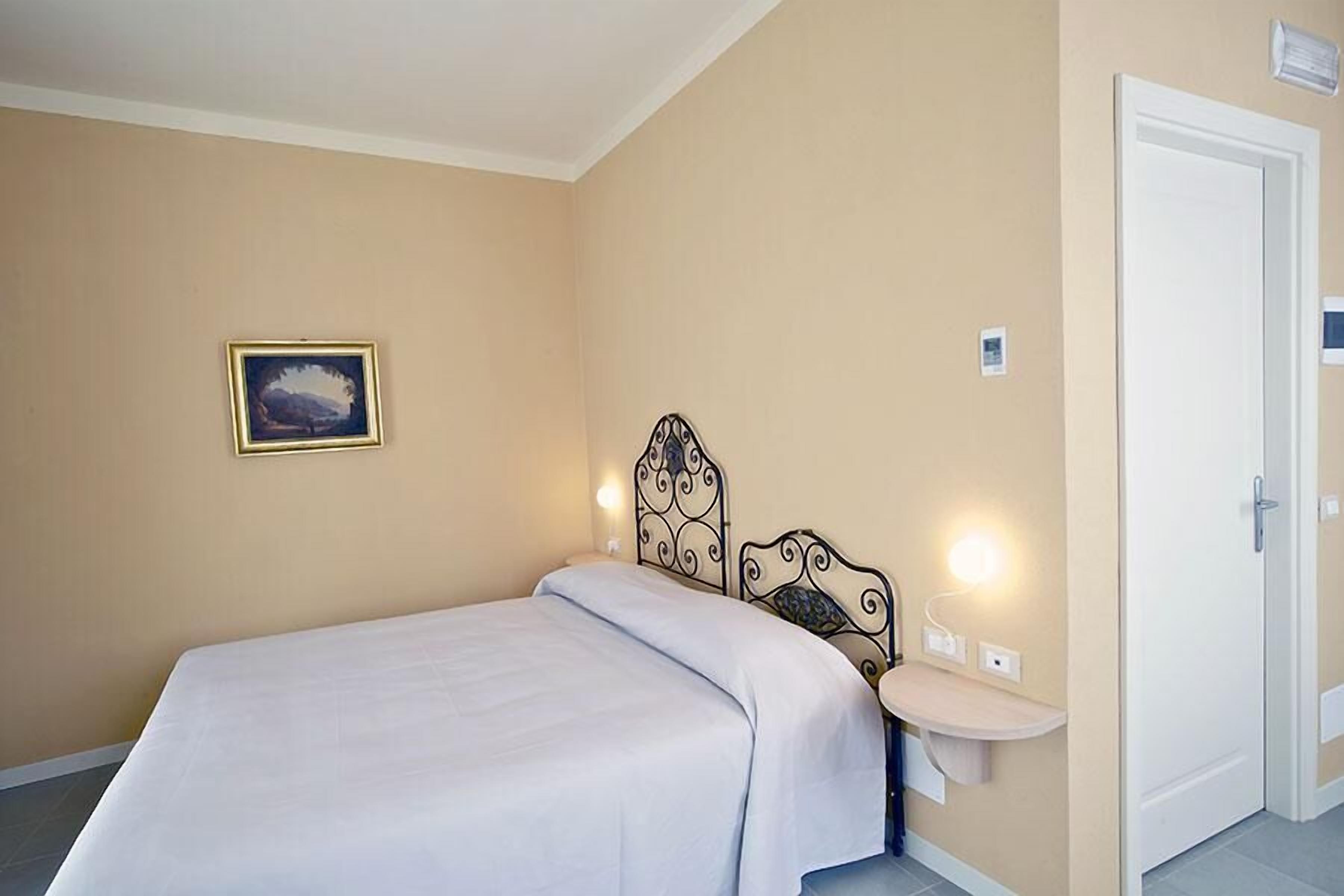 Une chambre à coucher comprenant un lit, une table de chevet, une étagère fixée au mur, une porte et un tableau encadré accroché au mur.
