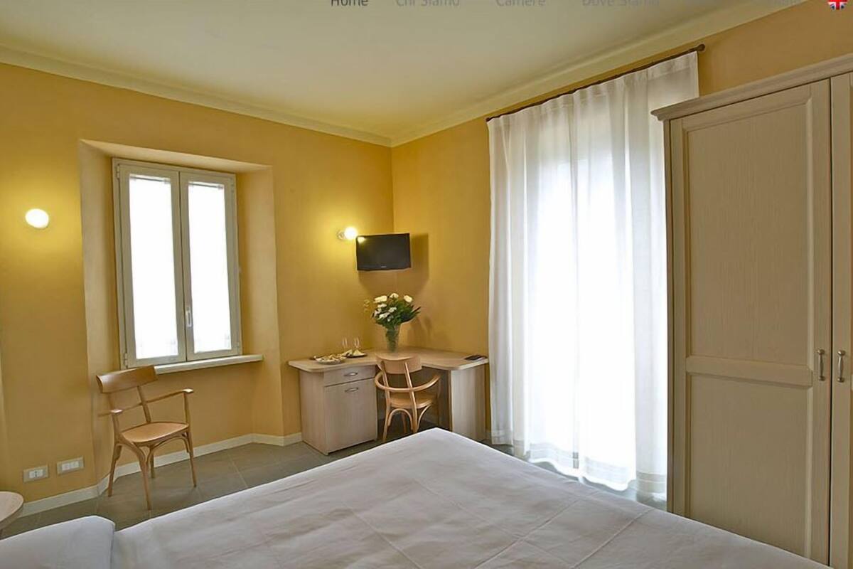 A hotel room with a bed, a desk with a chair, a TV mounted on the wall, and a window with curtains.