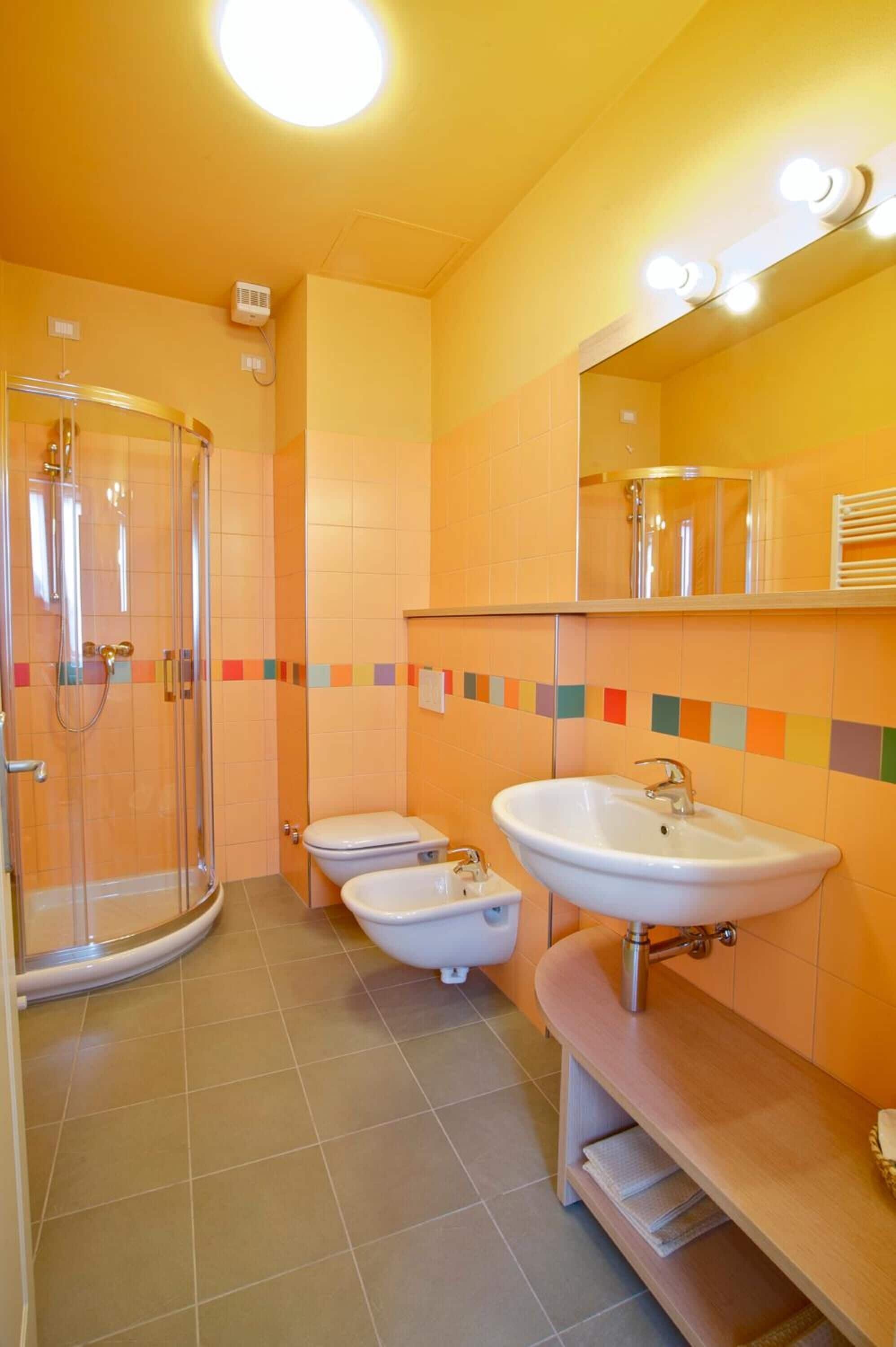 Ein Badezimmer mit Duschkabine aus Glas, zwei Toiletten, einem Waschbecken und einem beleuchteten Spiegel.