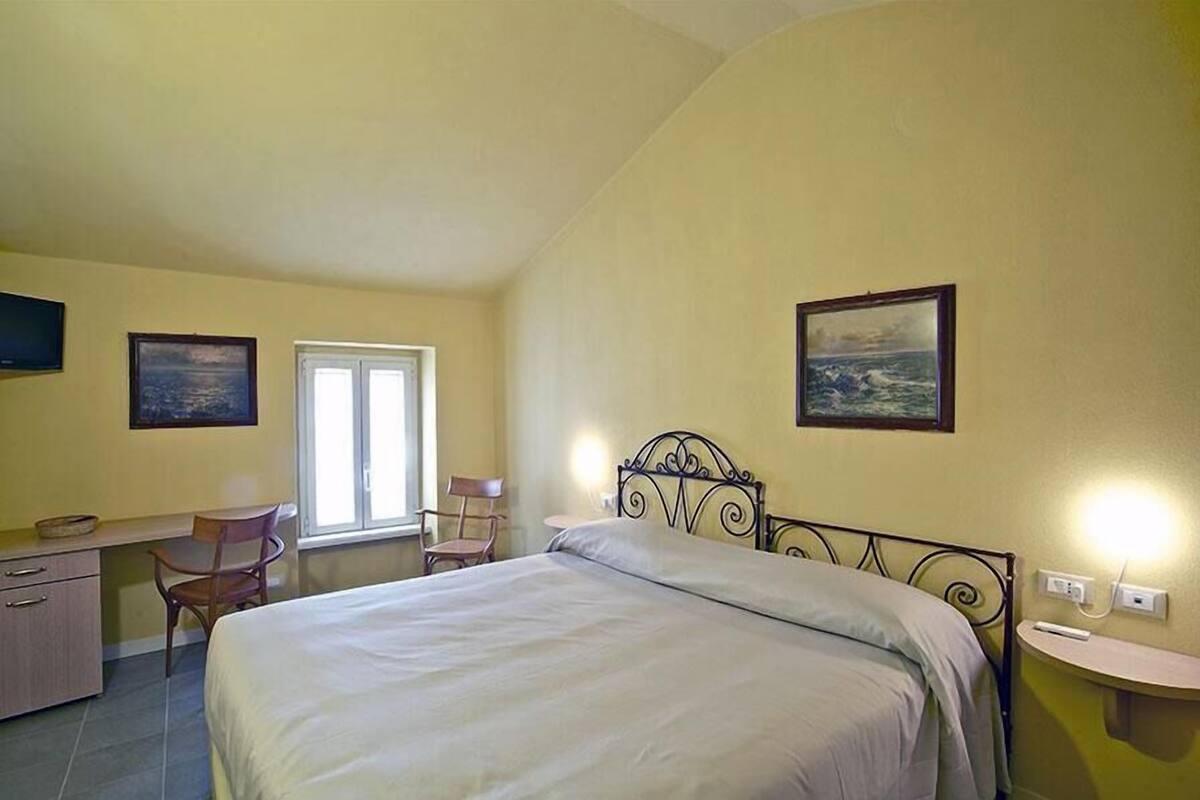 A bedroom with a bed, desk, chairs, and two paintings on the walls.