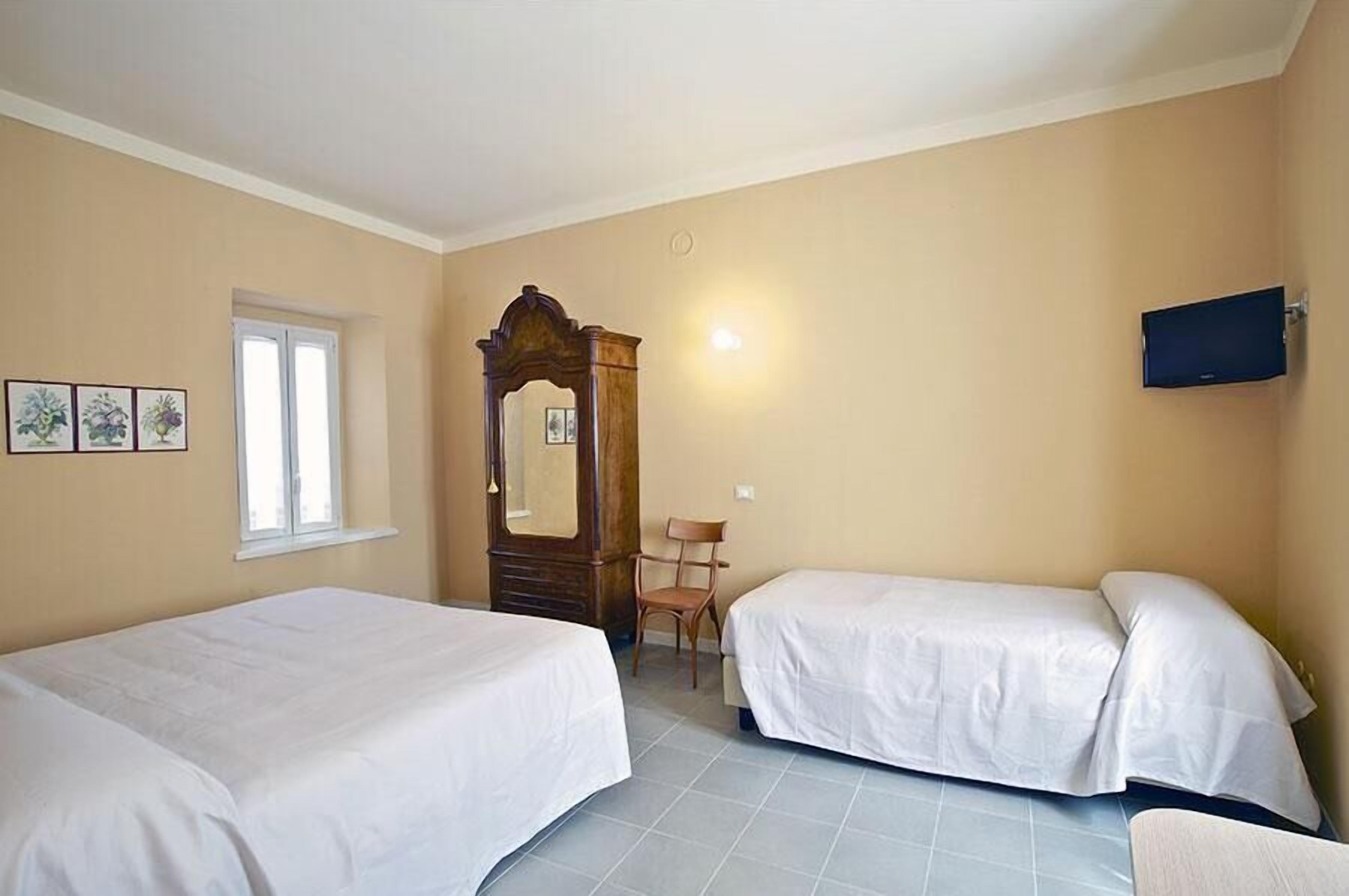 Ein Zimmer mit zwei Betten, einem Holzstuhl, einem Spiegel, einem Fernseher und einem Fenster.