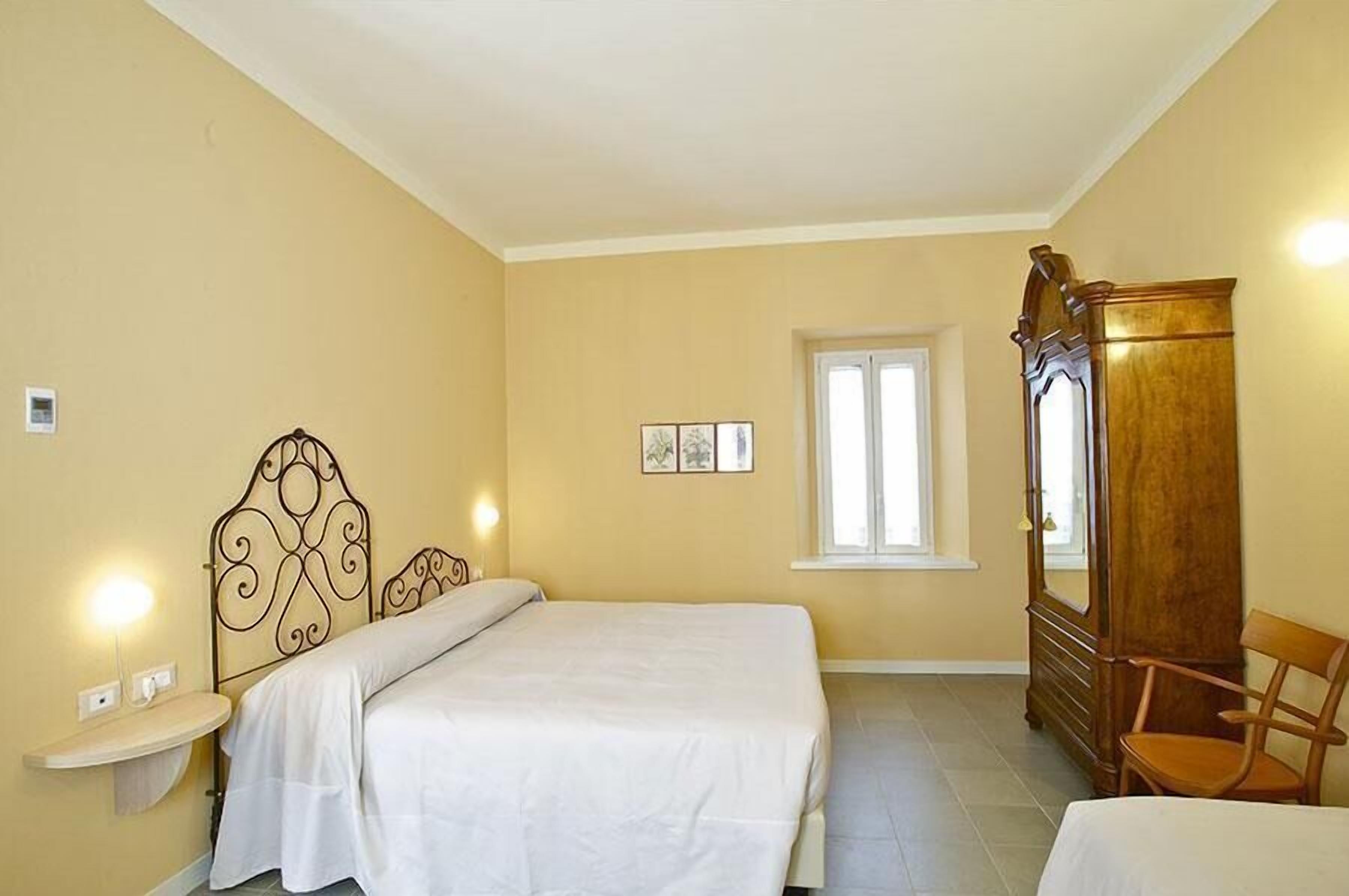 Un dormitorio con dos camas, un armario de madera, una silla, una mesita de noche y una ventana.