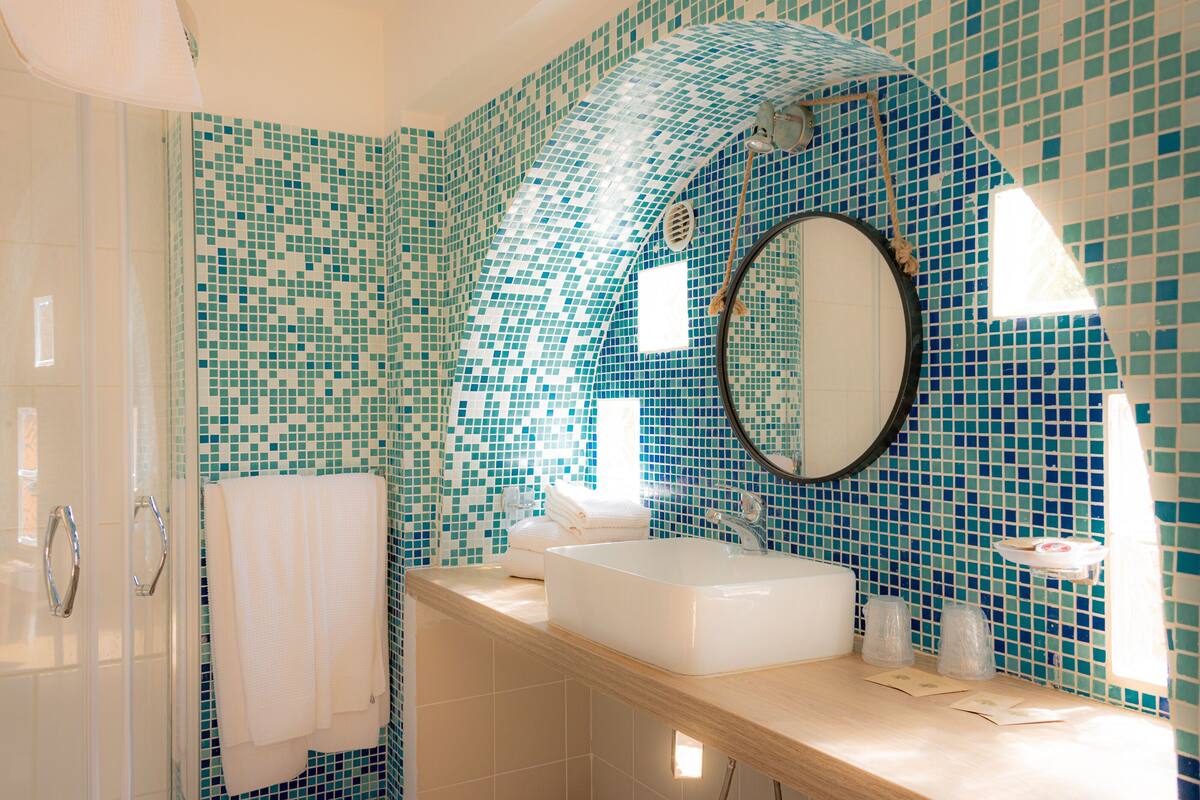 Une salle de bain avec un mur recouvert d’une mosaïque, un lavabo, un miroir et un espace douche.