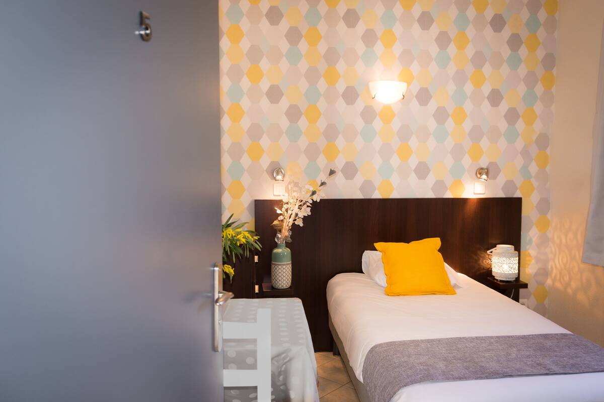 Une chambre d’hôtel avec un lit, une table de chevet, un vase de fleurs et un mur orné d’un motif géométrique.