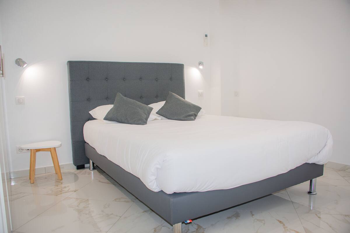 Une chambre à coucher moderne avec une tête de lit rembourrée de couleur grise, un matelas blanc et deux oreillers gris.