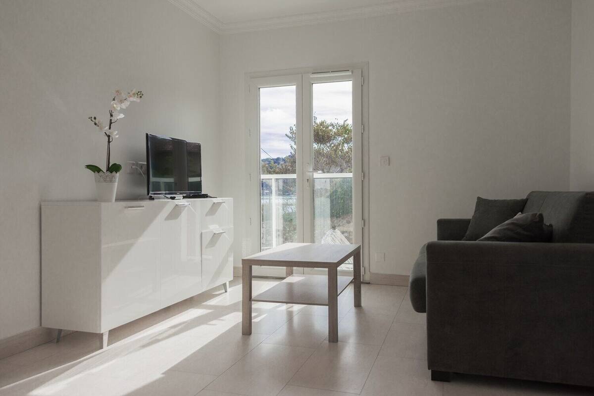 Un salon moderne avec un meuble blanc, une table en bois, un canapé gris et un téléviseur posé sur le meuble.
