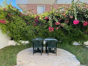 A patio with two green chairs and a table, surrounded by a stone floor and lush greenery with pink flowers. - Hôtel Reine D'Azur (Roquebrune-Cap-Martin)