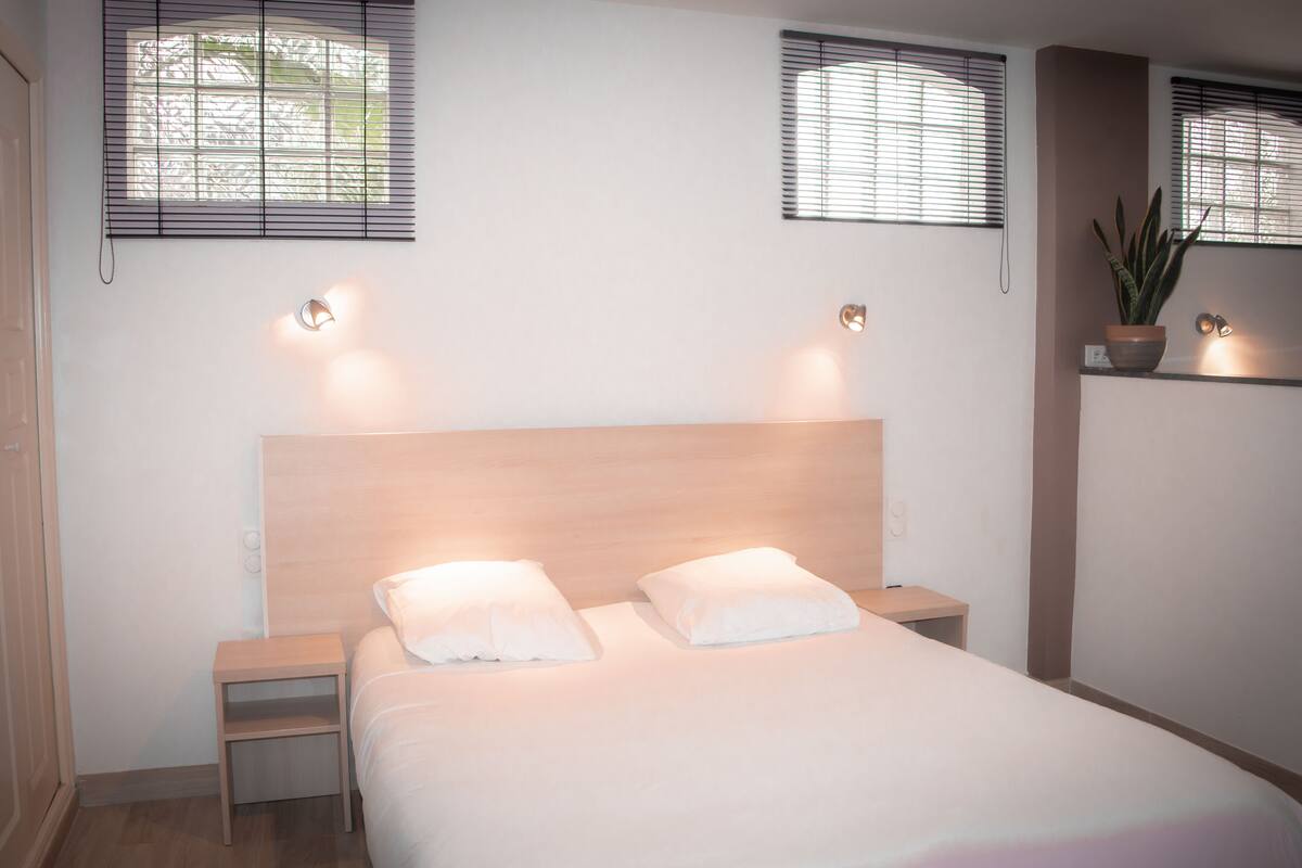 Une chambre à coucher bien rangée, avec une tête de lit en bois, deux tables de chevet et un grand lit recouvert de linge de lit blanc.