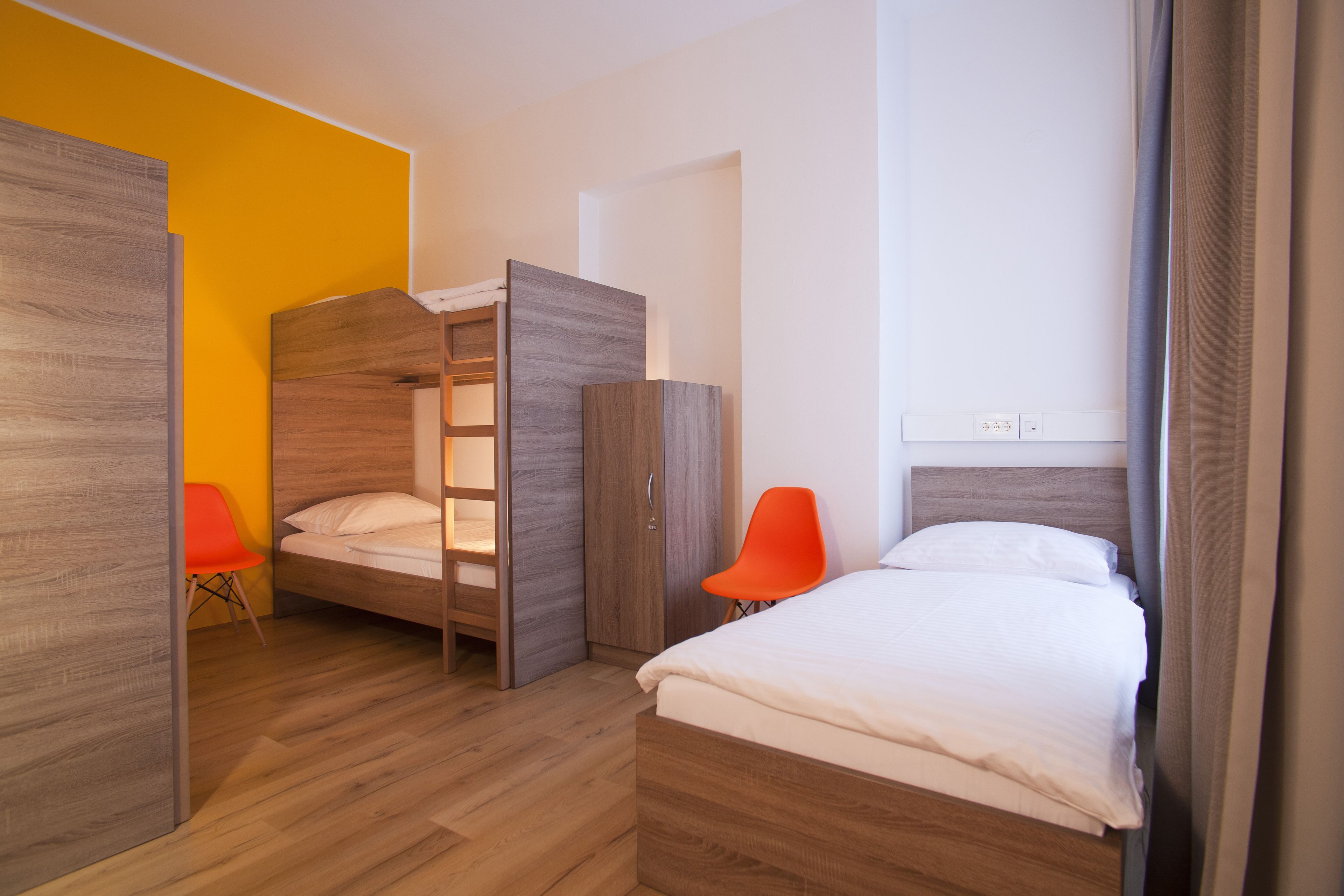 Ein modernes Hotelzimmer mit einem Holzbett, einem Einzelbett und einem leuchtend orangefarbenen Sessel.