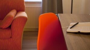A room with a wooden table, a red chair, a pair of brown shoes, and a lamp. - B&B HOTEL Maribor UNI Hostel (Maribor)