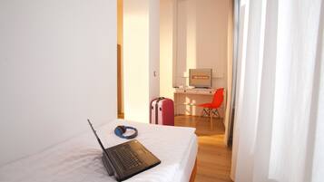 A hotel room with a bed, a laptop, headphones, a suitcase, and a desk with a chair.