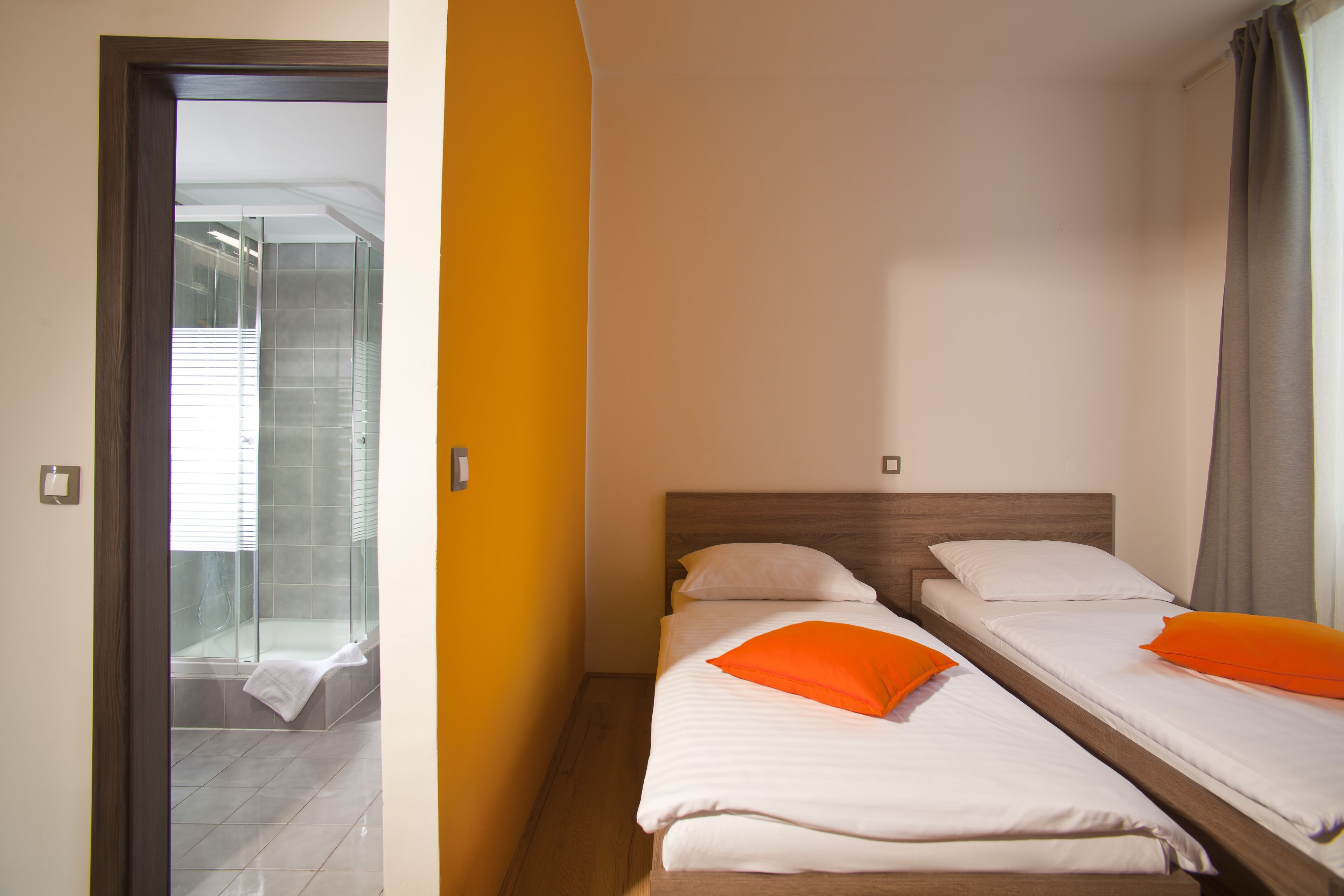 Habitación de hotel con dos camas, zona de ducha y puerta que da a un balcón.