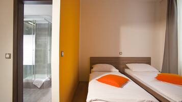 Habitación de hotel con dos camas, zona de ducha y puerta que da a un balcón.