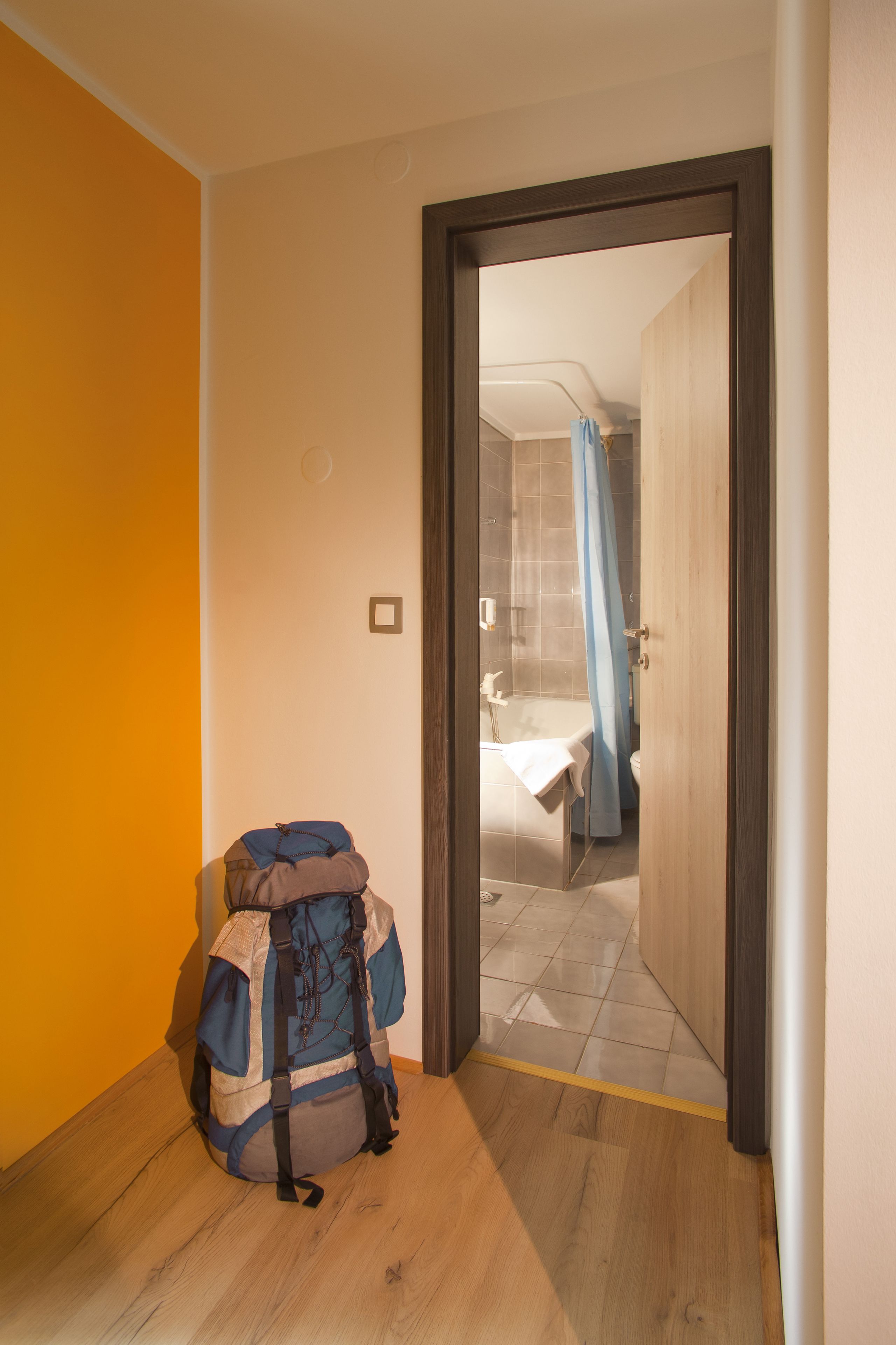 A hallway with a wooden floor, a backpack, and a bathroom visible through an open door.