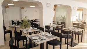 Un comedor amplio con varias mesas y sillas, paredes blancas y elementos decorativos como columnas y obras de arte en la pared.