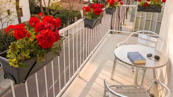 Ein Balkon mit Metallgeländern, einem runden Metalltisch, zwei Stühlen, einem Buch und einer Sonnenbrille auf dem Tisch.